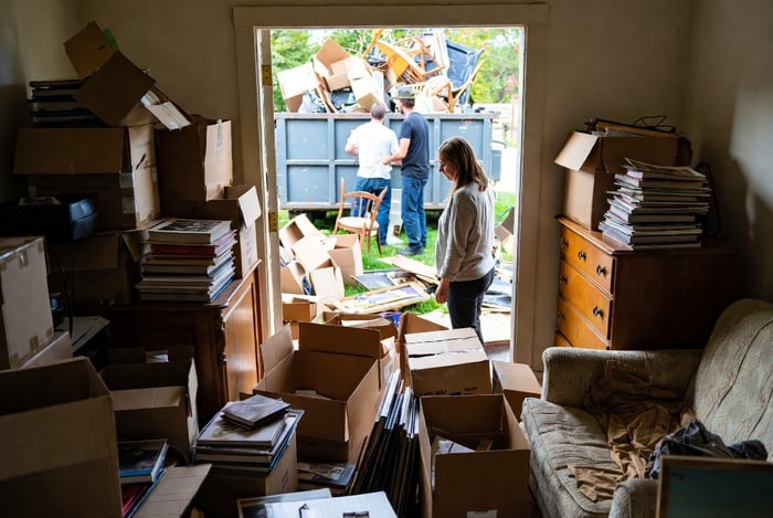 A cluttered living room and through a window you see household goods being tossed into a messy truck bed.